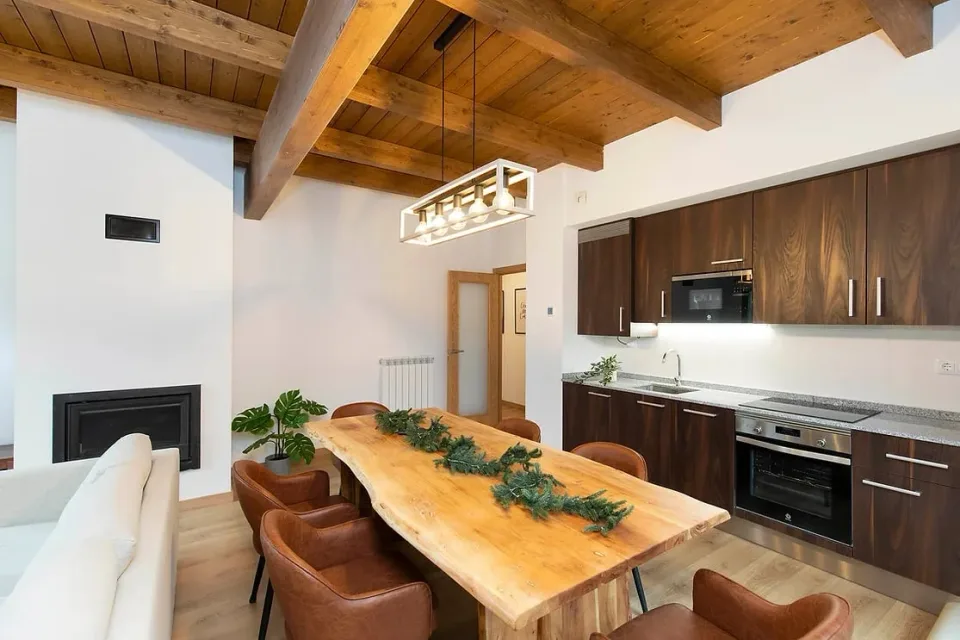 Dining area and open kitchen. The kitchen and dining table share an open space beneath wooden beams.